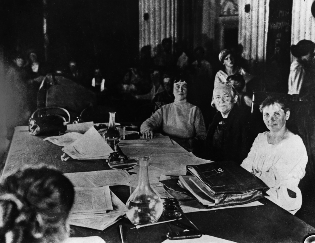 Foto von der Frauenkonferenz, Clara Zetkin sitzt mit Alexandra Kollontai und anderen Frauen an einem Tisch